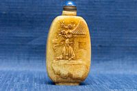 Front view of the rectangular jade snuff bottle showing a carved figure, tree, blossoms, and a small building with carved texture details.