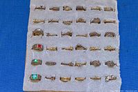 Photo showing all 36 gold plated blank ring settings arranged on foam padding, various sizes and styles including some with crystals and colored stones.