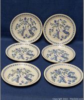 Front view of the six round ceramic plates arranged on dark blue fabric, displaying the colorful Lotte Turi design motifs with floral and figure elements.