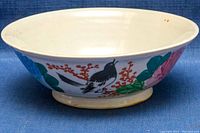 Side view of hand-painted porcelain bowl featuring a black bird on a branch with red berries and green leaves.
