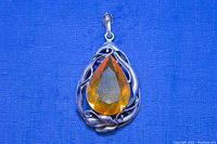 Front side of the antique sterling silver pendant showing detailed leaf and vine design and large pear shaped faceted amber-colored crystal.