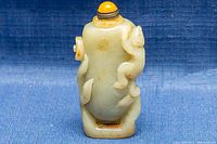 Front view of the carved jade snuff bottle showing embossed floral motifs and yellow stopper.
