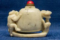 Front and side view showing carved embossed figures on pale jade bottle with red cap and open base
