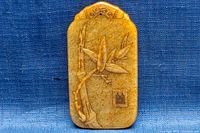 Front side of the jade pendant showing carved and embossed bamboo design on yellow-brown jade.