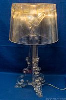 Full view of the clear polycarbonate lamp with pleated shade and ornate baroque base on blue background.