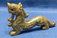 Front angled view of the green jade Qilin sculpture showing engraved details on the face, mane, and body with slight surface wear and natural stone veining.