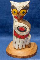 Front view of the owl carving showing carved and painted details with large yellow eyes and red accents.