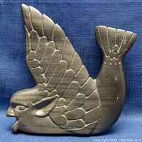 Front angled view of the dark stone carving showing creature's head, wings, and tail fin.