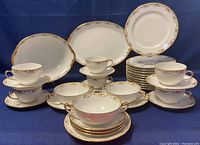Full display of porcelain set showing cups, saucers, bowls, plates, serving bowl, and platter with gold and floral trim.