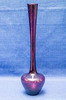 Front view of elongated purple glass bud vase with bulb base and narrow neck against blue background.