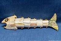 Side view of fish-shaped articulated bottle opener showing mother of pearl body sections and abalone tail with brass accents.