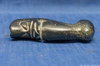 Side view of the black jade pendant showing engraved tribal design and polished surface with greenish spots.