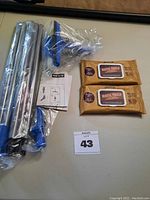 Photo showing parts of the window washer squeegee set including metal rods, blue handles, squeegee head, and two packets of furniture wipes.