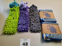 Three plush microfiber animal-shaped hand towels with heads in green, purple, and gray (dragon, unicorn, kitty) alongside two blue and white striped Norwex body and face pack towels.