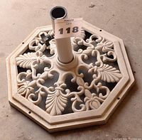 Top angled view of the decorative cast iron umbrella base showing intricate leaf and scroll patterns and central pole tube with securing knob