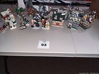 Full view of ceramic Christmas village set showing buildings, figurines, trees and fence pieces arranged on a table.