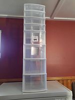 Full vertical view of white plastic storage unit with eight clear drawers, in good condition, positioned against a red wall and wooden paneling.