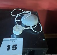 Google Mini smart speaker in gray fabric with white power cord and adapter shown on a black surface.