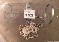 Top and side view of cylindrical wire mesh minnow trap with attached rope, showing snap closure mechanism.