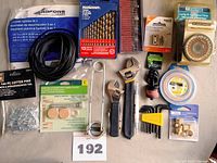 Photo showing various tools and hardware items including adjustable wrenches, drill bit set, screen spline coil, mechanical timer, wire coil, fasteners and small hardware kits.