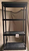 Black plastic resin four-tier shelving unit against a neutral backdrop with a label showing number 152.