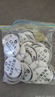 Photo of 20+ original 1960s anti Vietnam War pinback buttons in plastic bag showing peace symbols and text with some corrosion and discoloration visible.