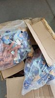Two plastic bags inside a cardboard box, each containing several Roadrunner plush toys from 1997 with visible tags, some dust and dirt inside bags.