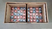Top view inside the open factory cardboard box showing two compartments each containing about 100 individually wrapped M&M red and blue yo-yos.