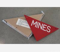 Sealed pack of 25 triangular metal landmine warning signs marked 'MINES'. Includes one loose sign placed on top as example.