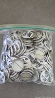 Photo showing large quantity of white and black reading 'SNOB FOR PEACE' pinback buttons inside a plastic bag.