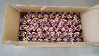 Top view of the large open cardboard box filled with multiple rows of red translucent Cherry Coke keychains.