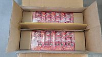 Open box showing two rows of 24 unopened Coca-Cola Santa playing card tins wrapped in plastic.