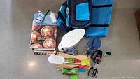 Various kitchen utensils, collapsible cooler bag, cookbooks, and manual hand mixer spread on floor
