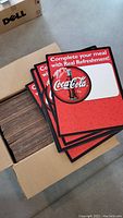 Box filled with stacked red Coca-Cola cardboard signs showing logo and slogan.