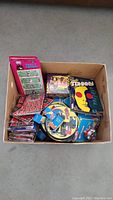 Box containing mixed new old stock collectibles including comic books, cards, and keychains