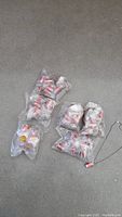 Three sealed plastic bags containing multiple mini Coca Cola can keychains and necklaces on a grey surface.