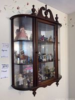 Front angle view of wooden and glass wall mounted display cabinet showing ornate top design and multiple shelves.