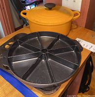 Overview photo showing yellow Le Creuset Dutch oven with lid and two black cast iron baking molds on wooden surface.