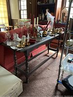 Full view of the dark painted console table placed in front of a red sofa, with various small items displayed on top.
