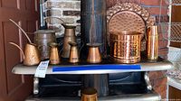 Overview photo showing multiple copper tone serve ware items including pitchers, pot, and Gregorian stamped platter on a shelf.