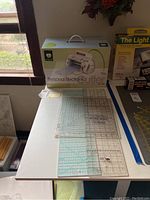 Cricut Personal Electronic Cutter in original box on table with three quilting measuring boards in front of and beside it.