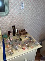 Overview of collection of dollhouse miniatures on a white dresser with patterned wallpaper background