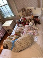 Crocheted sheep, teddy bear, cloth bunny dolls and assorted dolls arranged on bed