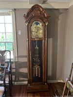 Full front view of oak tall-case grandfather clock with arched bonnet top, full-length glass door, brass weights and pendulum