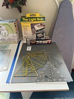 Full view showing The Light Box in original box, custom sealing iron box, cutting mat, and multiple clear plastic quilt rulers placed on the mat