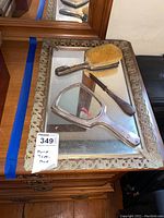 Overview of the mirrored tray with the brush, hand mirror, and fingernail tool placed on top. Tray has ornate silver-tone edging and mirrored surface.