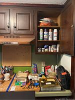 Wide view of the crafting tools lot showing shelves with cans of paint, adhesives, and array of tools and supplies spread on a table.
