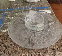 Top view showing the glass crudites platter with etched fruit pattern, central bowl with leaf handles, and six small cocktail glasses arranged around the platter.
