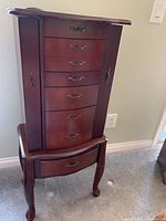 Front view of tall standing jewelry cabinet showing multiple drawers and side doors closed.