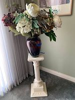 Full view of faux flower arrangement in vase sitting on stone pedestal near window